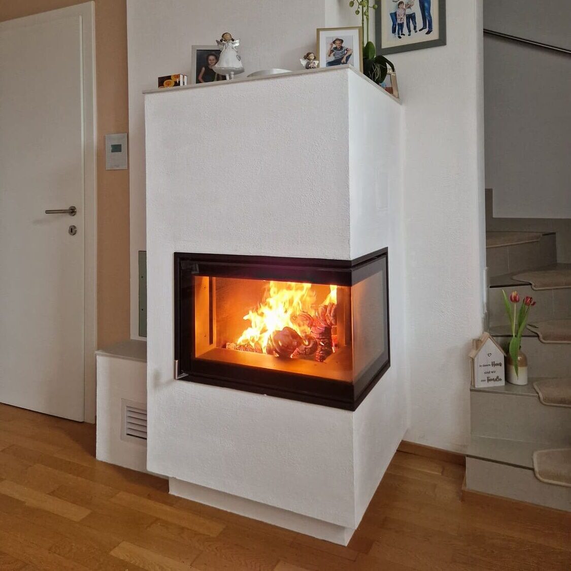 Moderner Kachelofen perfekt integriert in einer weißen Wand, der Boden ist aus Holz