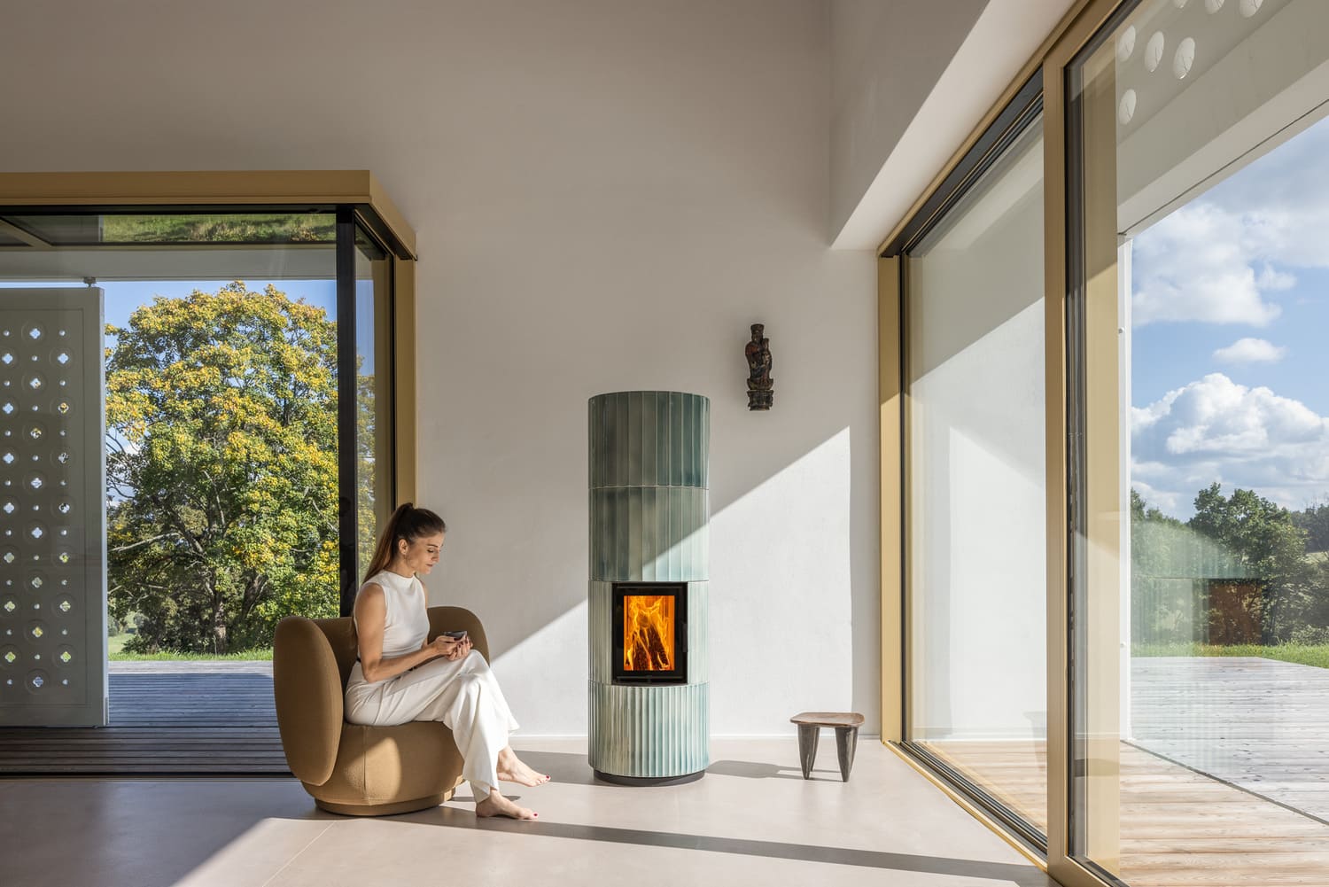 Moderner Grüner Hoxter Blox Ofen in einem modernen Haus. Eine Frau sitzt davor in einem braunen Stuhl und hält eine Tasse in den Händen