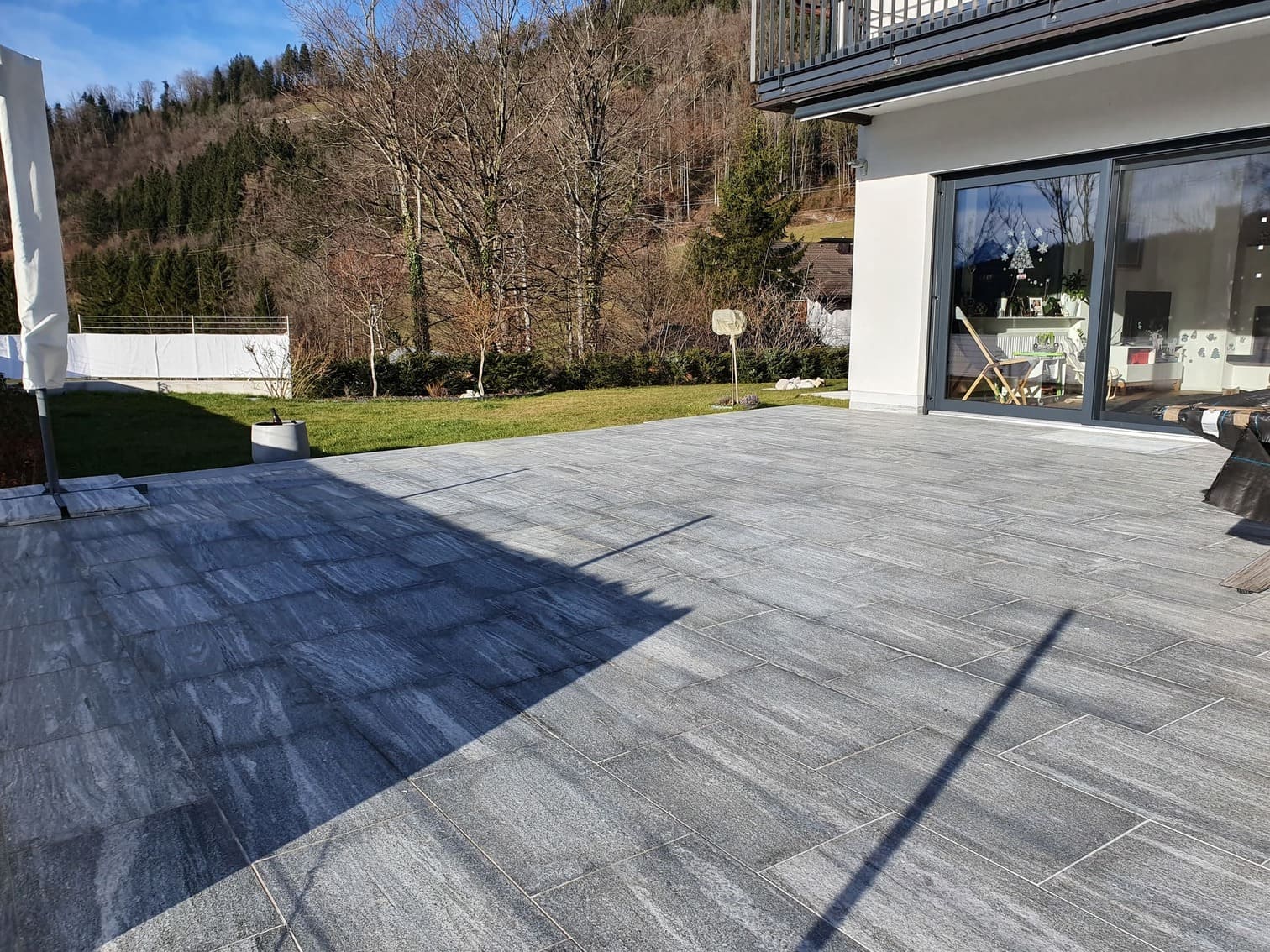Großer Außenbereich der komplett gefliest wurde, dahinter sieht man eine Wiese und Bäume
